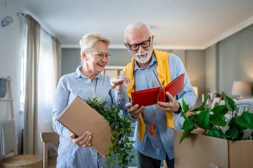 A senior couple reminisces over a photo album together as they pack cardboard boxes to move.