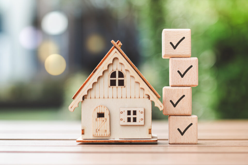 A small model house next to wooden blocks with check marks to resemble a moving checklist.